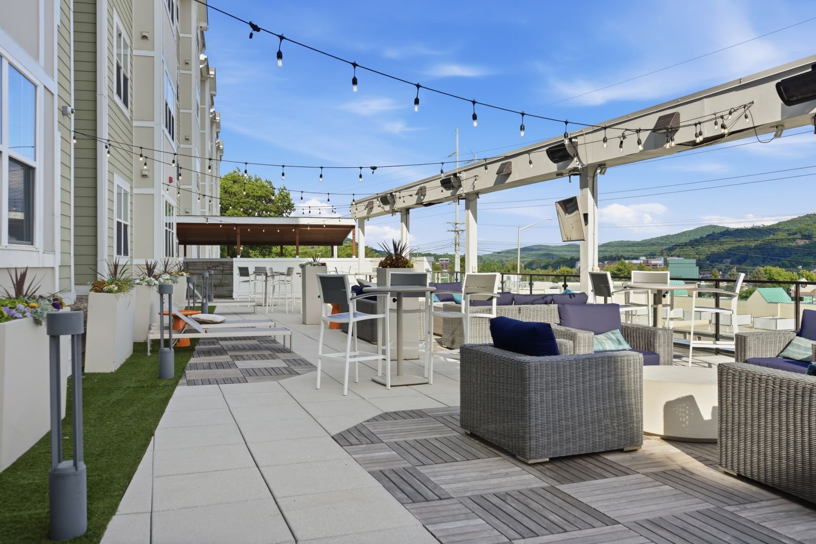 Rooftop lounge with comfortable outdoor seating, string lights, covered bar area, and scenic mountain views, creating an inviting space to relax and socialize.